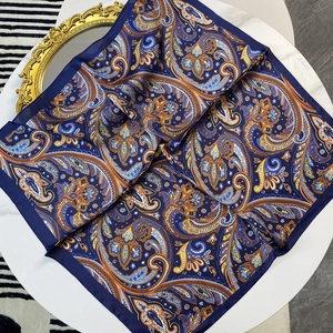 70cm blue paisley silk satin square scarf folded on white table with gold mirror background