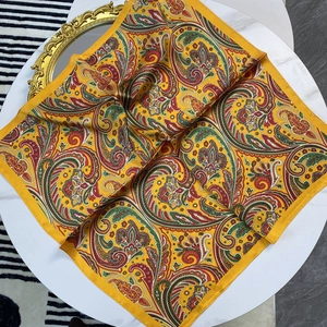 Square silk scarf with vintage paisley patterns in yellow on a white table