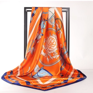 Carré en soie à motif carrosse orange et bleu présenté sur un présentoir en métal noir