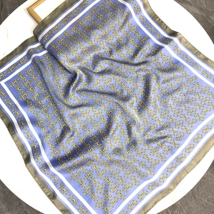 Sky blue satin square scarf with golden horsebit chain print on a white table