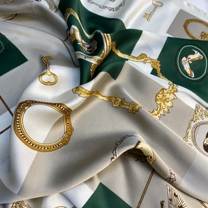 Gros plan d'un foulard carré en soie avec motifs de chaînes dorées sur fond vert