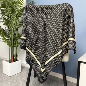 Carré de soie élégant 70cm avec imprimé géométrique noir et doré sur une chaise blanche