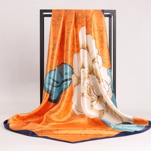 Orange floral silk satin square scarf with navy blue edges draped on a black stand