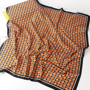 Detail eines Seidenquadrats mit orangem Blumenmuster und Buchstabendruck auf glattem Stoff