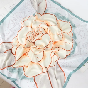 Detailed macro shot of orange floral print silk scarf with mint green hem and soft drapes