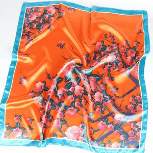 Close-up of glossy orange satin silk scarf featuring pink floral patterns and blue borders