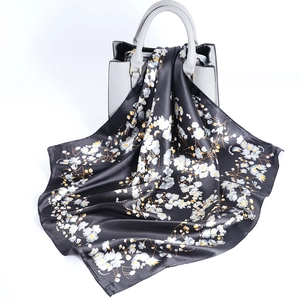 Black floral satin scarf with yellow blossoms draped over a gray leather handbag