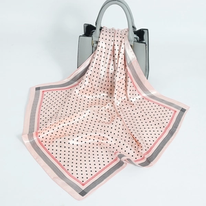 Pink polka dot satin square scarf with striped borders tied on a grey handbag