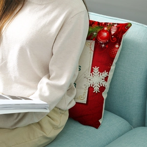 Red Christmas pillow cover featuring snowflake and ball patterns on a blue sofa