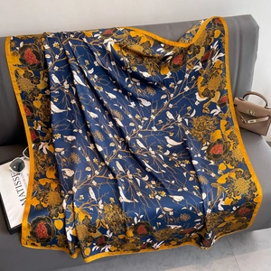 Navy blue satin silk shawl with floral pattern and gold border on a grey sofa