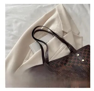 Detail view of large brown monogram tote bag with sturdy handles on a beige blazer