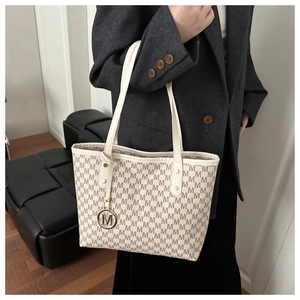 Detail of cream tote bag featuring repeating M print and gold letter charm accessory