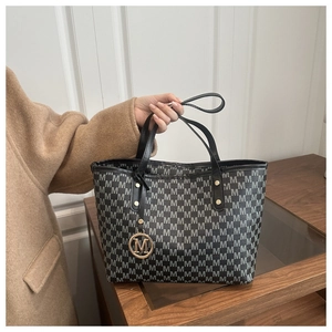 Detail of monogram M print tote bag with metallic pendant and leather handle on wood