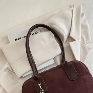 Détail du sac cabas en daim bordeaux avec poignées en cuir sur fond blanc texturé