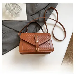 Dettaglio della borsa a tracolla in pelle marrone con patta intrecciata e fibbia dorata