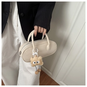 Detail of off-white baguette bag with plush charm and silver zipper held by model