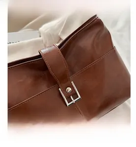 Gros plan du sac cabas en cuir marron montrant la boucle métallique et les coutures