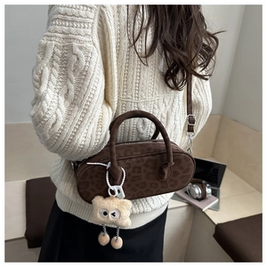 Brown leopard print suede cylinder bag with white plush charm worn on shoulder