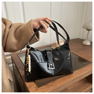 Détail d'un grand sac cabas noir en cuir brillant avec un charm en perles de bois