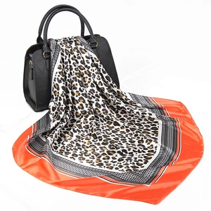 Satin silk scarf with leopard print and orange border draped over a black handbag