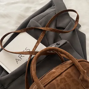 Detail van bruine matte Boston-tas met handvatten en schouderriem op een platte achtergrond