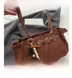 Detail of brown frosted suede handbag featuring a decorative buckle and wooden bead strap