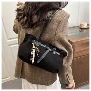 Detail of black matte suede shoulder bag featuring a bohemian beaded charm and leather strap