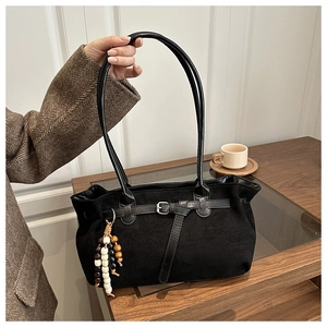 Detail of matte black suede handbag with ethnic wood bead charm and buckle strap