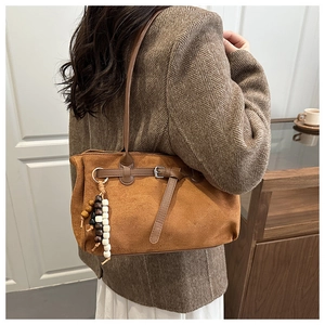 Close-up of caramel suede tote bag with metal buckle and decorative beaded tassel charm