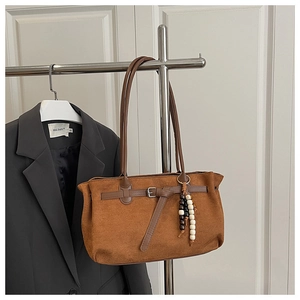 Close-up of brown suede handbag with decorative silver buckle and beaded bag charm