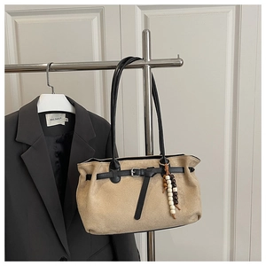Close-up of khaki suede tote bag with black leather handle and wooden bead charm accessory