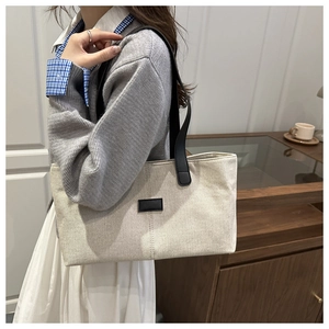 Close-up of beige canvas tote bag with black leather straps and minimalist center patch
