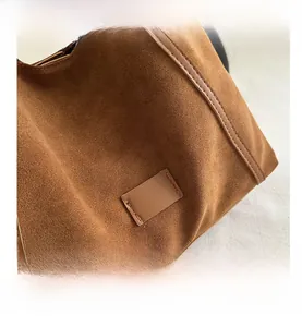Detailed close-up of brown frosted leather tote bag with contrast stitching and retro patch