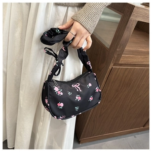 Détail d'un sac d'épaule en nylon noir avec motifs floraux roses et poignée froncée