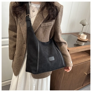 Detail of a black suede hobo bag with adjustable strap worn with a brown blazer
