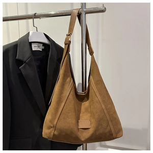 Detail of caramel suede tote bag with adjustable strap on a silver display stand