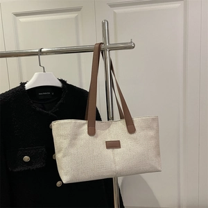 Minimalist canvas tote bag with brown leather handles and decorative trim in cream white