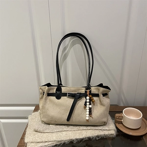 Beige canvas tote bag with black leather straps and colorful wooden bead accessory
