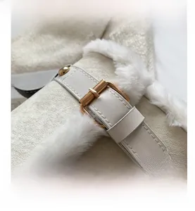 Detail of beige suede handbag featuring white faux fur trim and gold metal buckle strap