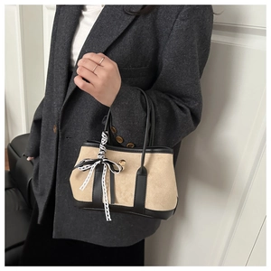 Détail du sac beige en daim avec garniture en cuir noir et nœud en dentelle