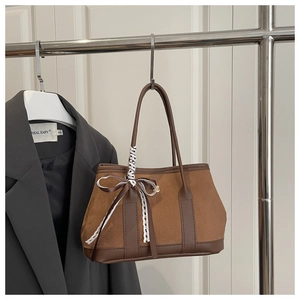Close-up of brown suede tote bag featuring lace bow details and long leather handles
