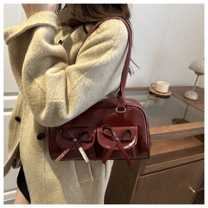 Detail of burgundy leather shoulder bag with bow accents on two front pockets