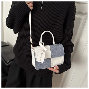 Detail of color-block bag showing white leather and blue denim stitching with a metal clasp