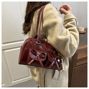Detail of dark red underarm bag with bow pockets and beaded charms on the shoulder strap