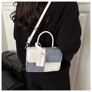 Detail shot of the contrast color leather and denim square bag worn by a model