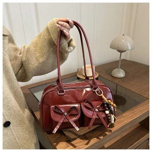 Close-up of deep red glossy underarm bag featuring decorative bows and a beaded charm