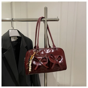 Detail of dark red glossy handbag featuring front bow pockets and beaded charm accent