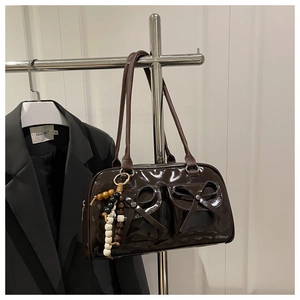 Detail of dark brown patent leather handbag with bow pockets and colorful beaded charm