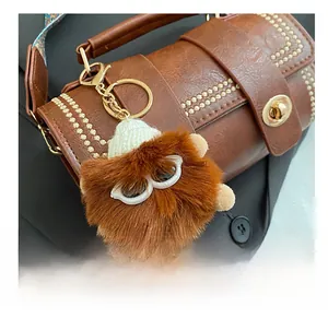 Close-up of a brown fluffy monster doll charm with a knit hat on a leather Boston bag