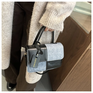 Detail of color-block crossbody bag with double handles and fashion tag in model's hand